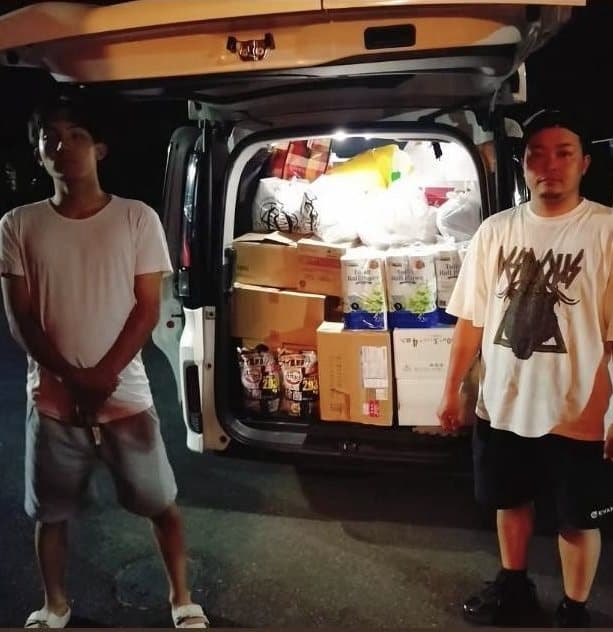 夜、物資を積み込んだ車の後ろに立つ2人