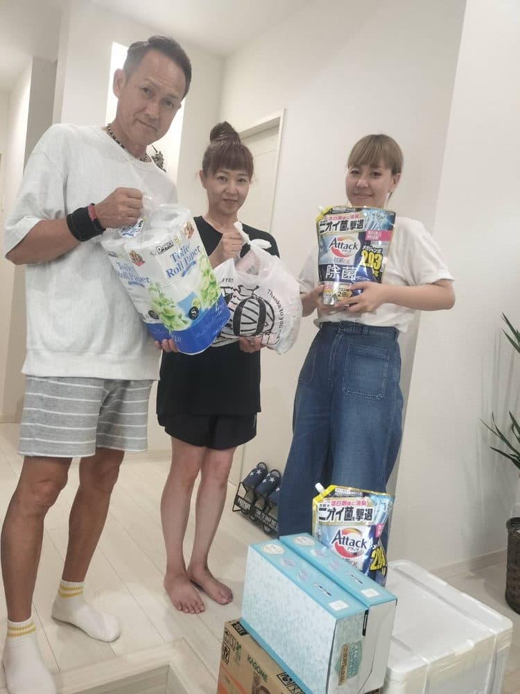 玄関先で、トイレットペーパーや洗剤を手にした3人
